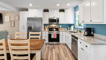 Una cocina moderna con armarios blancos, electrodomésticos de acero inoxidable, una mesa de comedor de madera y una pared de acento azul.