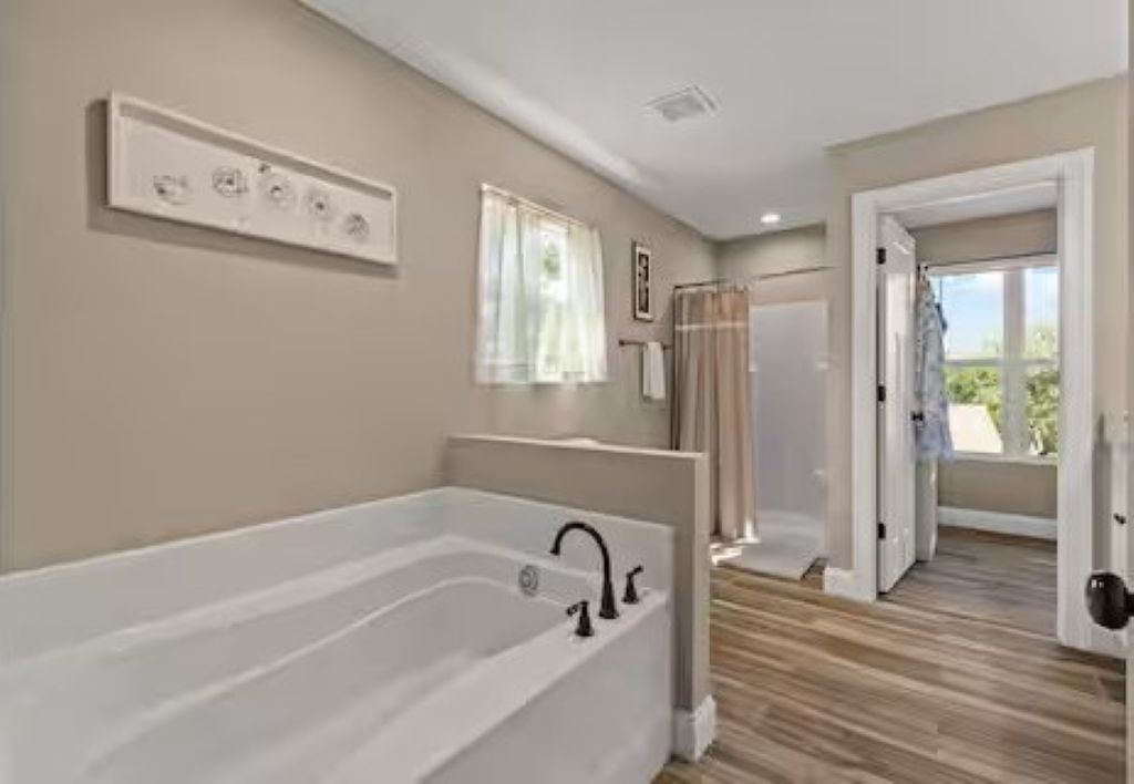 A bathroom with a large bathtub, a shower area, and a window providing natural light.