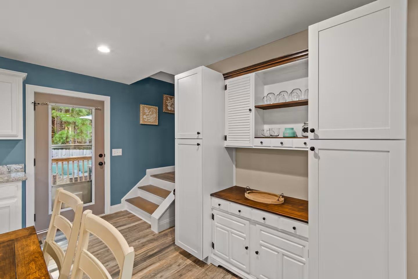A kitchen with white cabinets, a wooden countertop, and a view of the outdoors through a door.