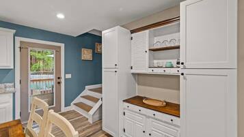 A kitchen with white cabinets, a wooden countertop, and a view of the outdoors through a door.