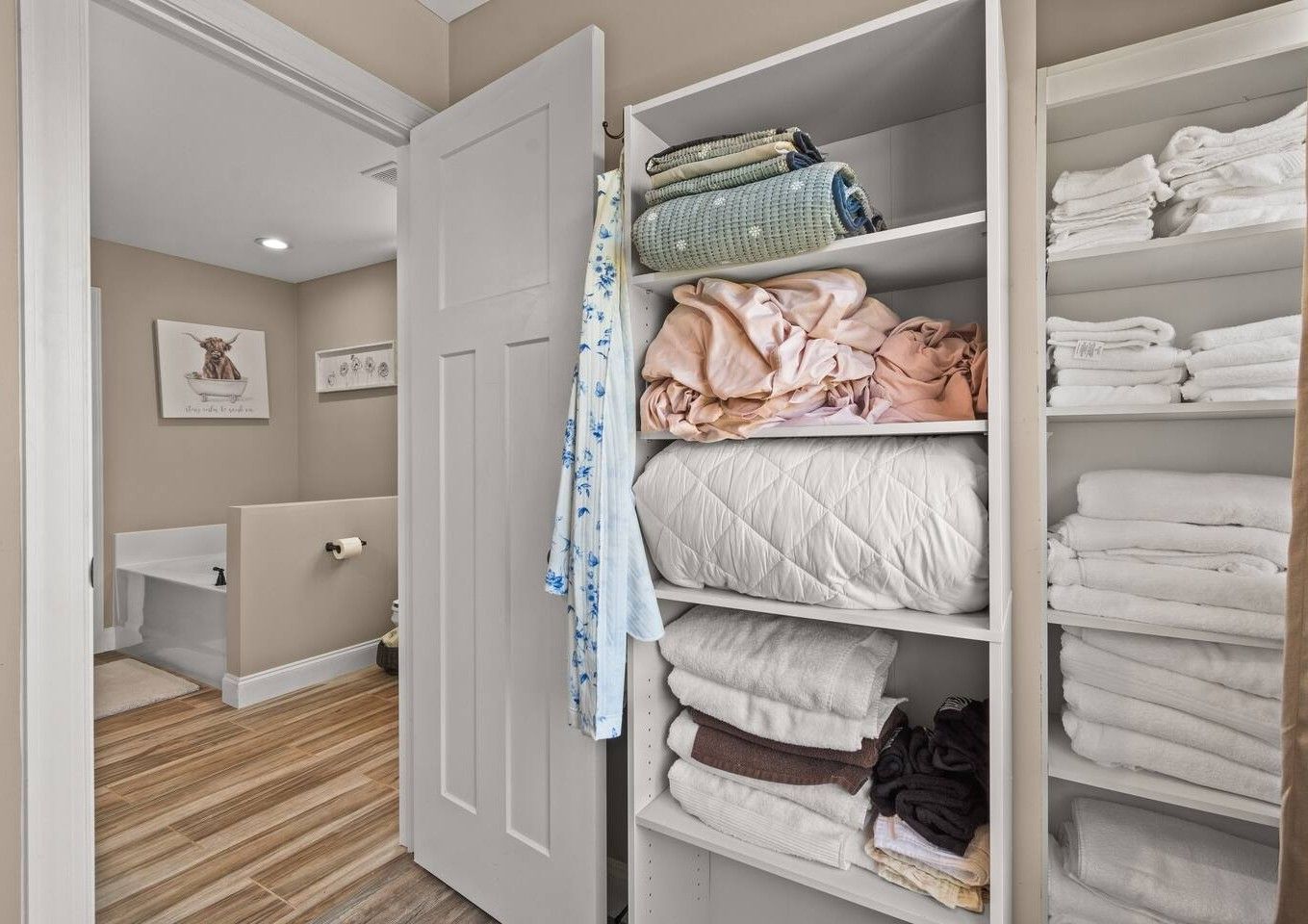Een inloopkast met planken voor handdoeken en een deur naar een badkamer.