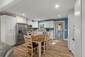 A modern kitchen with white cabinets, a stainless steel refrigerator, and a wooden dining table with chairs.