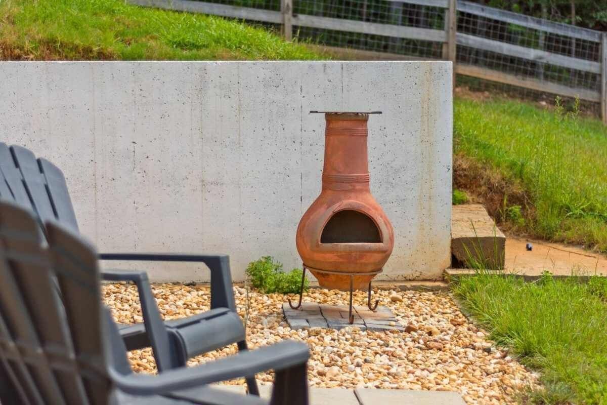 A rustic outdoor seating area with a concrete wall, a metal fire pit, and a gravel path.