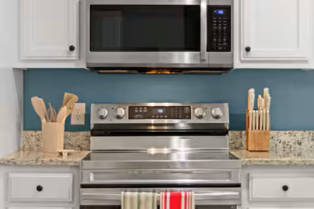 A kitchen with a stainless steel microwave, oven, and a set of knives on the counter.