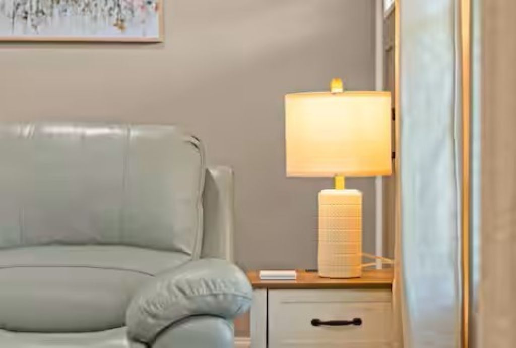 A room with a light-colored sofa, a bedside table with a lamp, and a wall-mounted artwork.