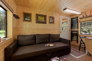 Ein Holzblockhaus-Innenraum mit einer Couch, gerahmten Bildern, einem Fenster und einer Tür.