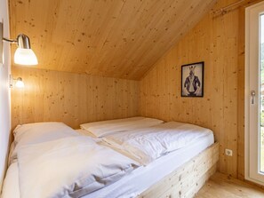 Une chambre dans une cabane en bois, avec deux lits, une lampe fixée au mur et un tableau encadré.