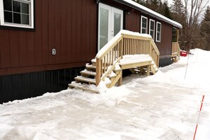 A wooden deck leading to a cabin with a snow-covered ground.