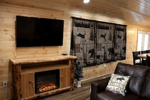 A wooden interior with a flat-screen TV mounted above a fireplace, a large forest-themed curtain, and a leather sofa with a decorative pillow.
