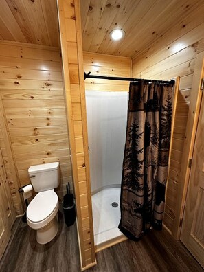 A wooden cabin bathroom with a toilet, shower, and a curtain with a forest pattern.