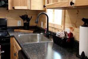 A kitchen with wooden cabinets, a stainless steel sink, a black faucet, and a countertop with a black basket containing items.