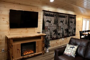 A wooden interior with a flat-screen TV mounted above a fireplace, a large forest-themed curtain, and a leather sofa with a decorative pillow.