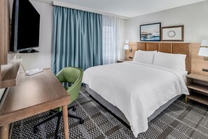 Quarto de hotel com cama, escrivaninha, cadeira, televisão e janela com cortinas.
