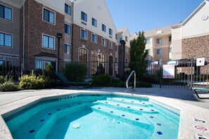 Uma piscina com degraus de acesso, cercada por uma grade e um edifício com várias janelas e fachada de pedra.