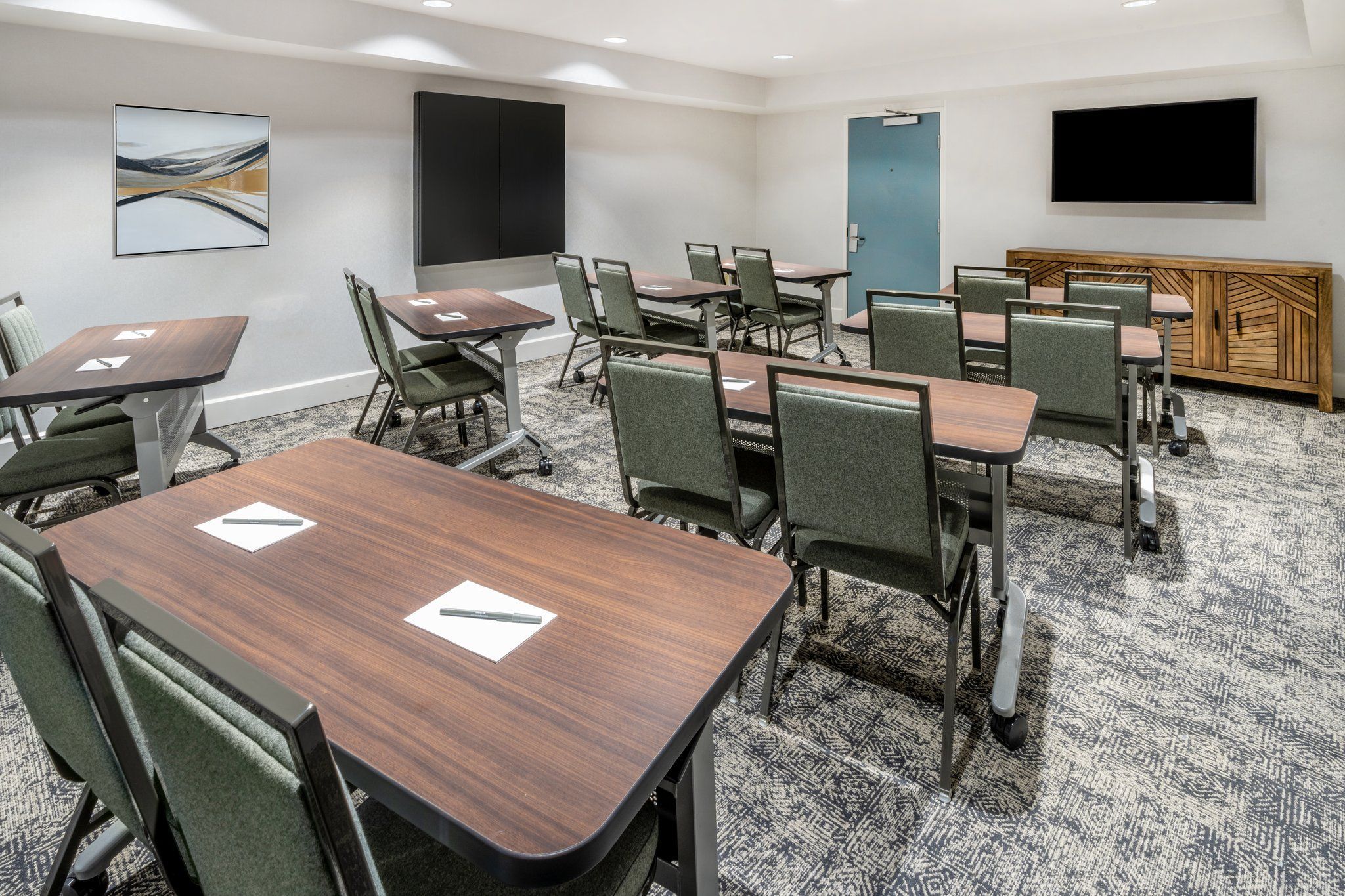 A conference room with multiple tables and chairs, a large flat-screen TV, and a wooden cabinet.