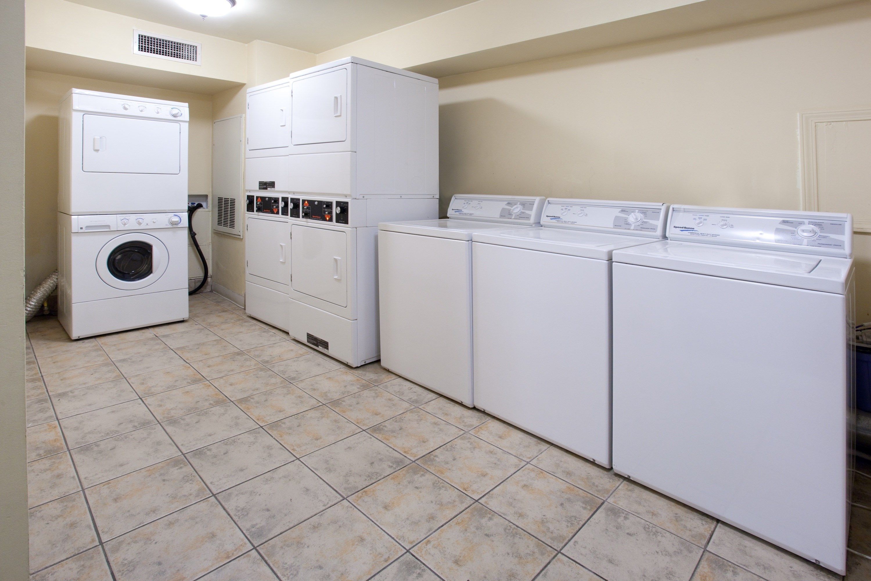 A laundry room with stacked washers and dryers, a vent, and a tiled floor.