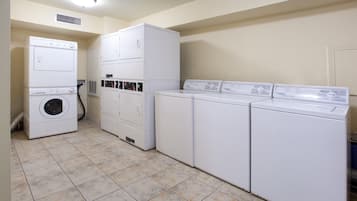 A laundry room with stacked washers and dryers, a vent, and a tiled floor.