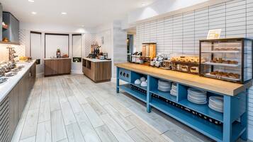 A modern kitchen with a wooden counter, blue shelves, and a display case with pastries.