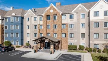 A multi-story hotel with a central entrance, parking lot, and a clear blue sky.
