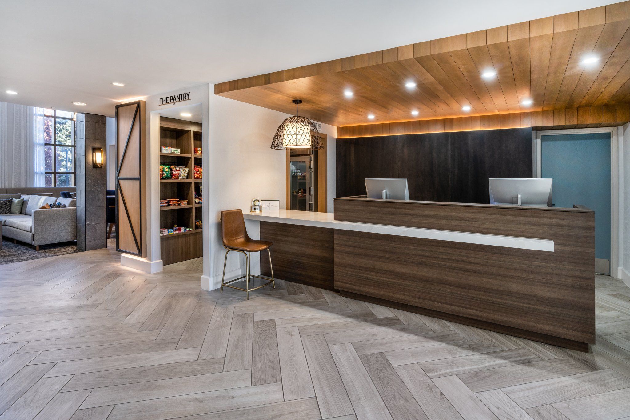 A modern reception area with a wooden reception desk, a laptop, and a sign reading 'THE PANTRY.'