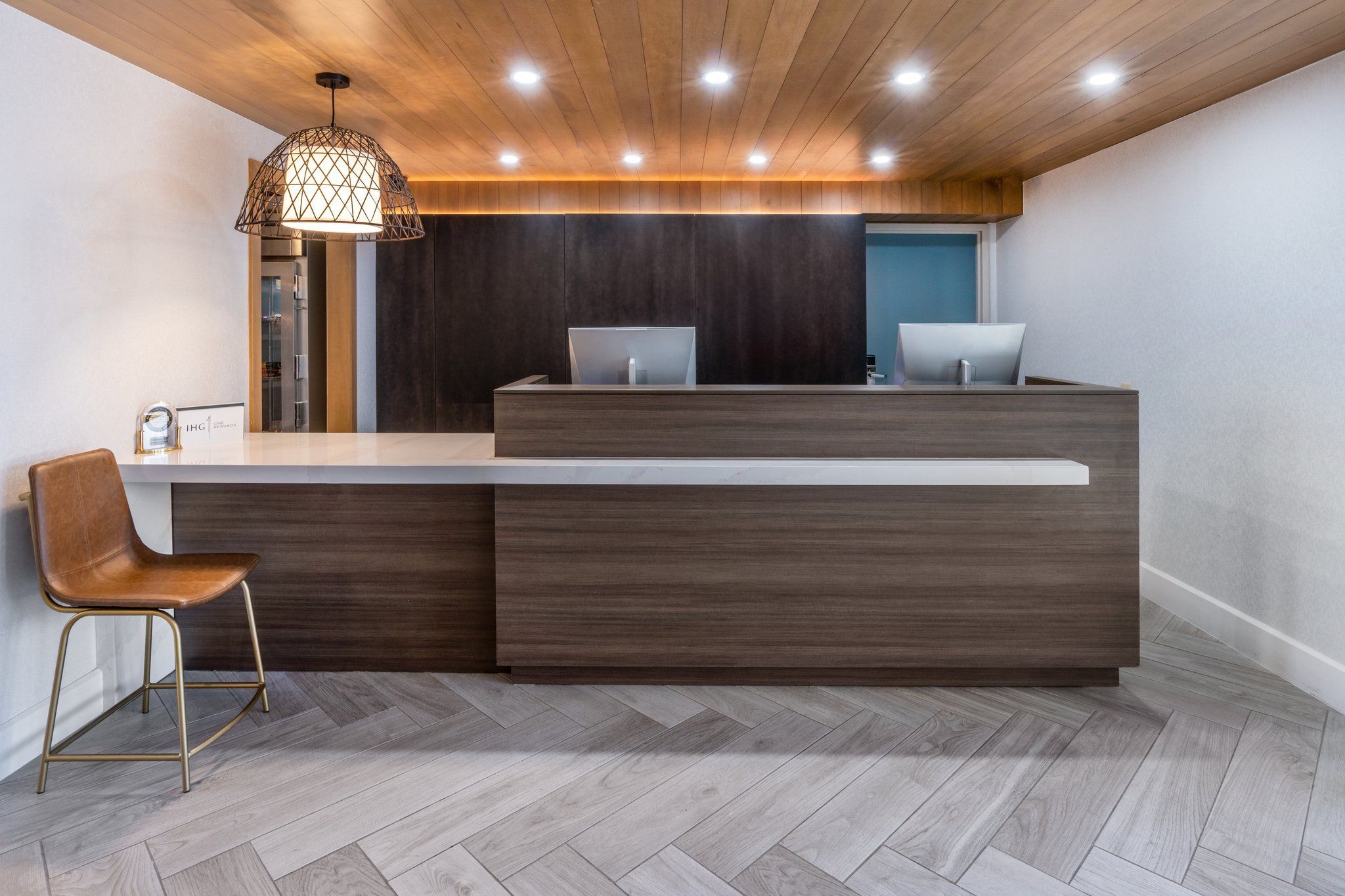 A reception desk with two computer monitors, a wooden ceiling, and a herringbone-patterned floor.