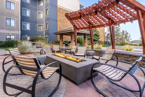An outdoor seating area with a fire feature, lounge chairs, and a pergola structure.