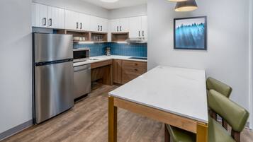 Een moderne keuken met een roestvrijstalen koelkast, houten kasten, een witte aanrecht en een eettafel met groene stoelen.