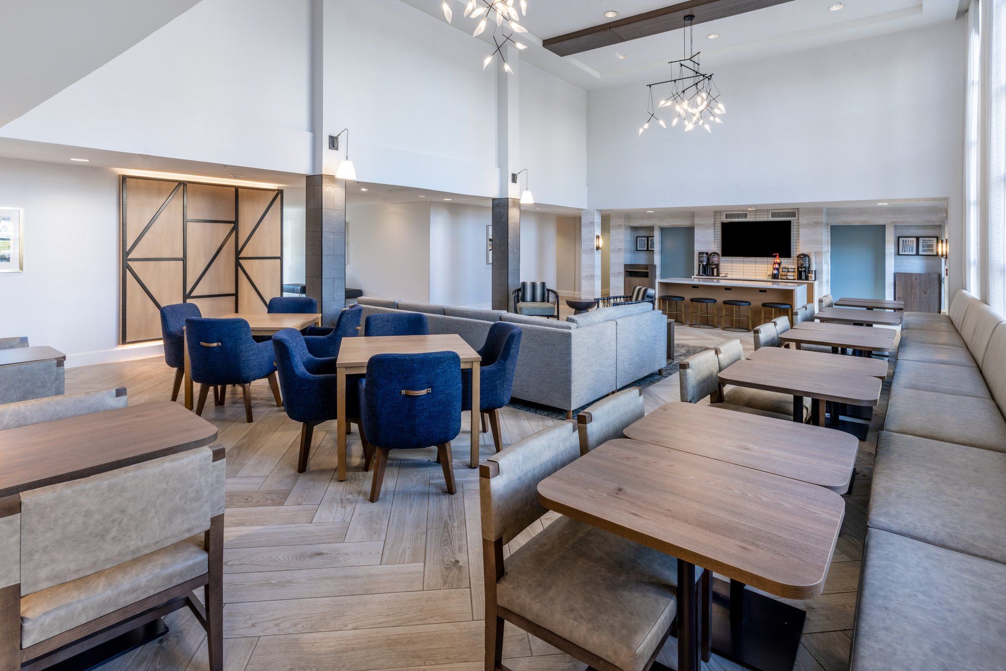 A modern restaurant with high ceilings, wooden tables, blue chairs, and a bar area.