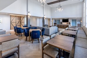 A modern restaurant with high ceilings, wooden tables, blue chairs, and a bar area.