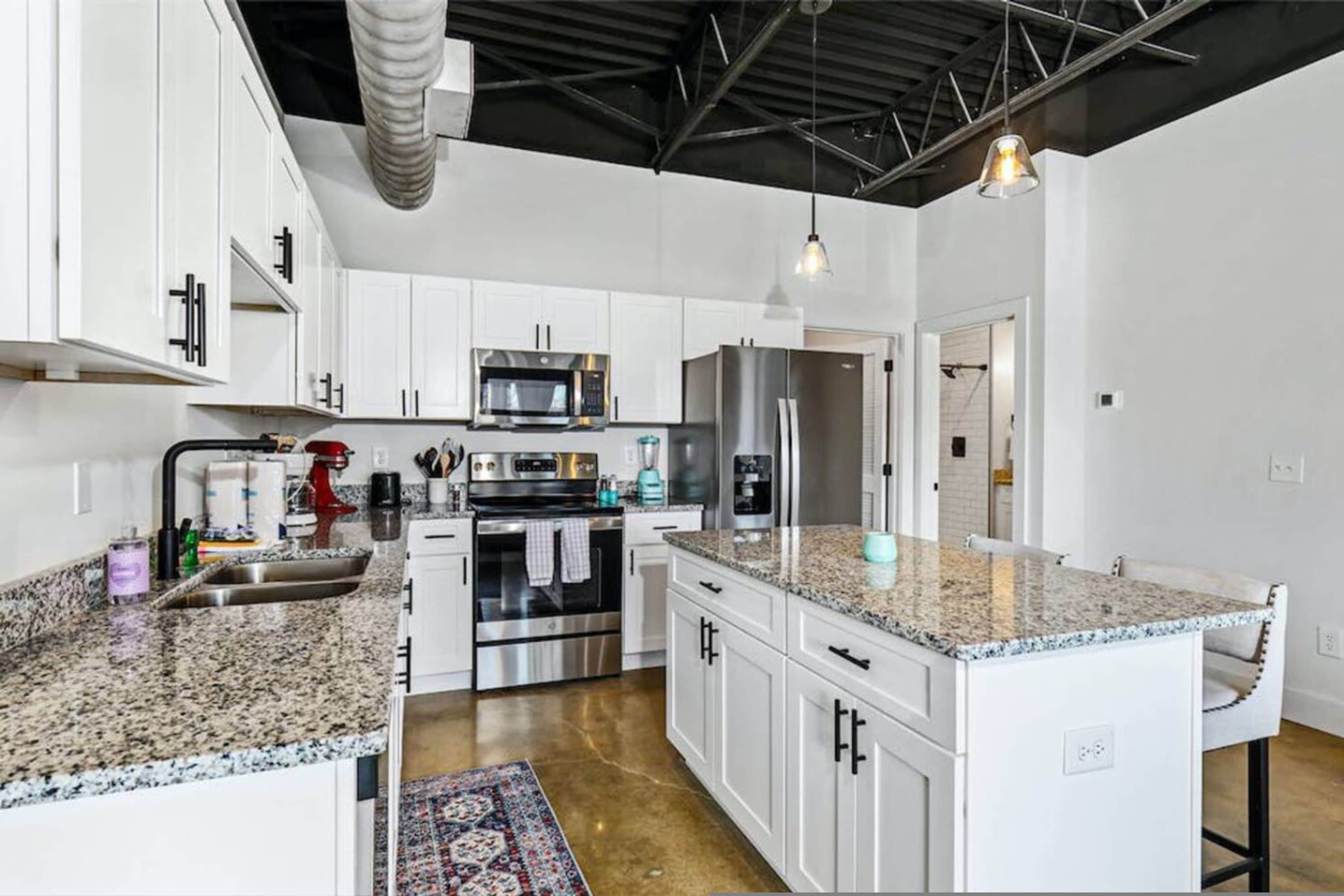 A modern kitchen with white cabinetry, stainless steel appliances, granite countertops, and a central island.