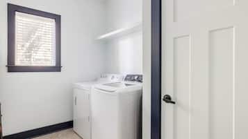 A laundry room with a washing machine and dryer, a window with blinds, and a door.