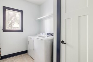 A laundry room with a washing machine and dryer, a window with blinds, and a door. - Central Nashville Oasis 3BR 3BA Sleeps 10 (Nashville)