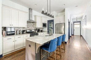 A modern kitchen with white cabinetry, a central island with bar stools, stainless steel appliances, and a tiled backsplash. - Central Nashville Oasis 3BR 3BA Sleeps 10 (Nashville)