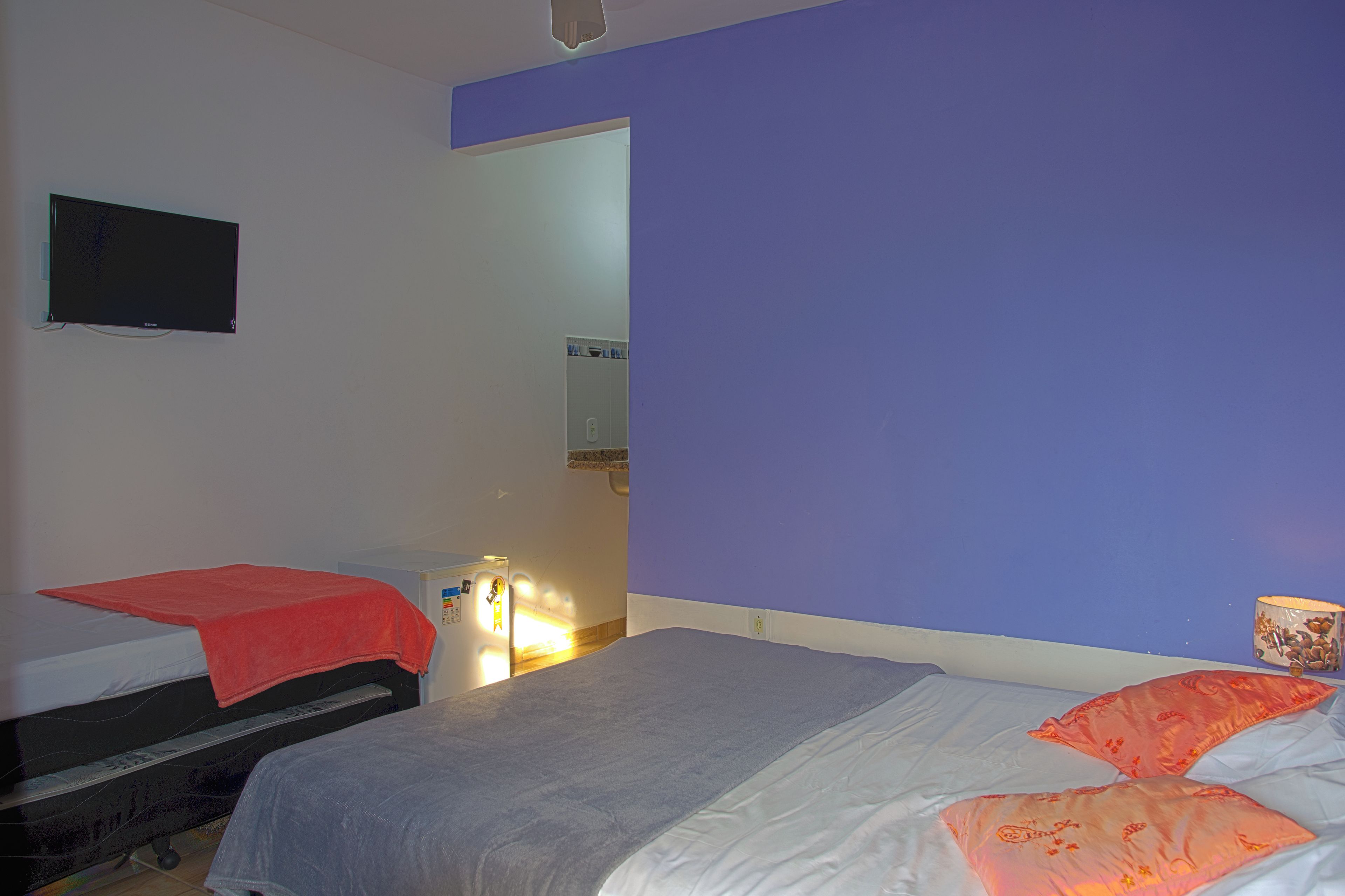 Un dormitorio con dos camas, un televisor en la pared y un baño visible a través de una puerta abierta.