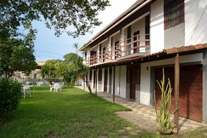 A two-story building with a balcony, a paved walkway, and a grassy area with outdoor furniture. - Pousada Prisco Peró (Cabo Frio)