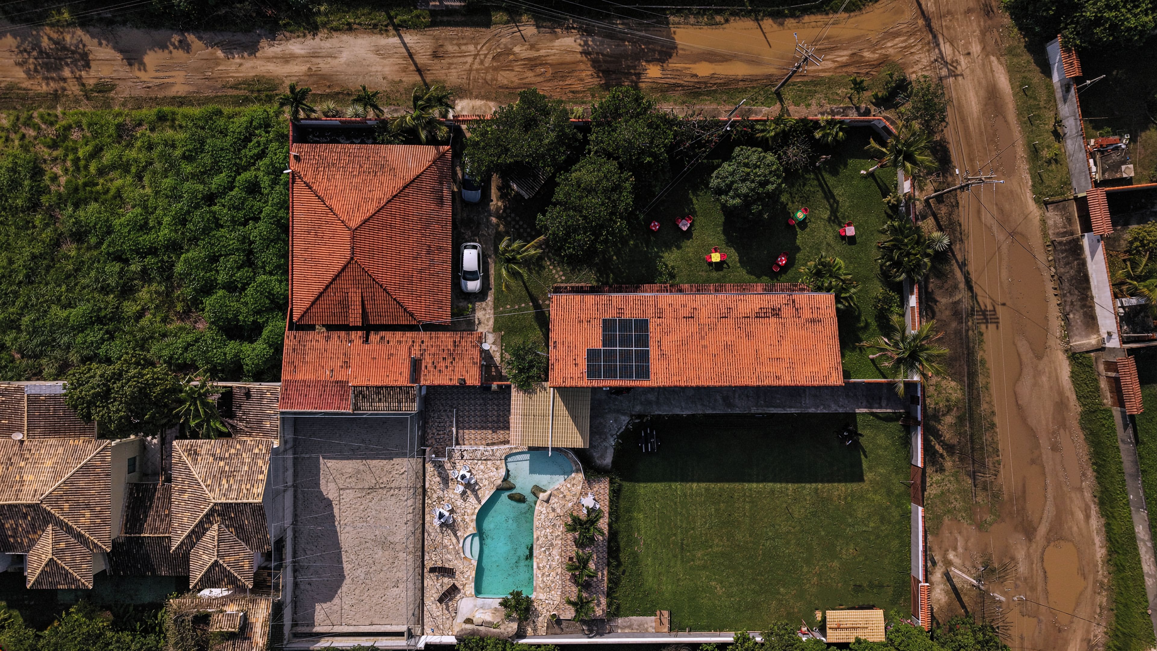 Vista aérea de una zona residencial que incluye una piscina, un automóvil y un panel solar en un tejado.