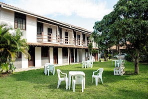 A building with a covered outdoor seating area, multiple windows, and a tree. - Pousada Prisco Peró (Cabo Frio)