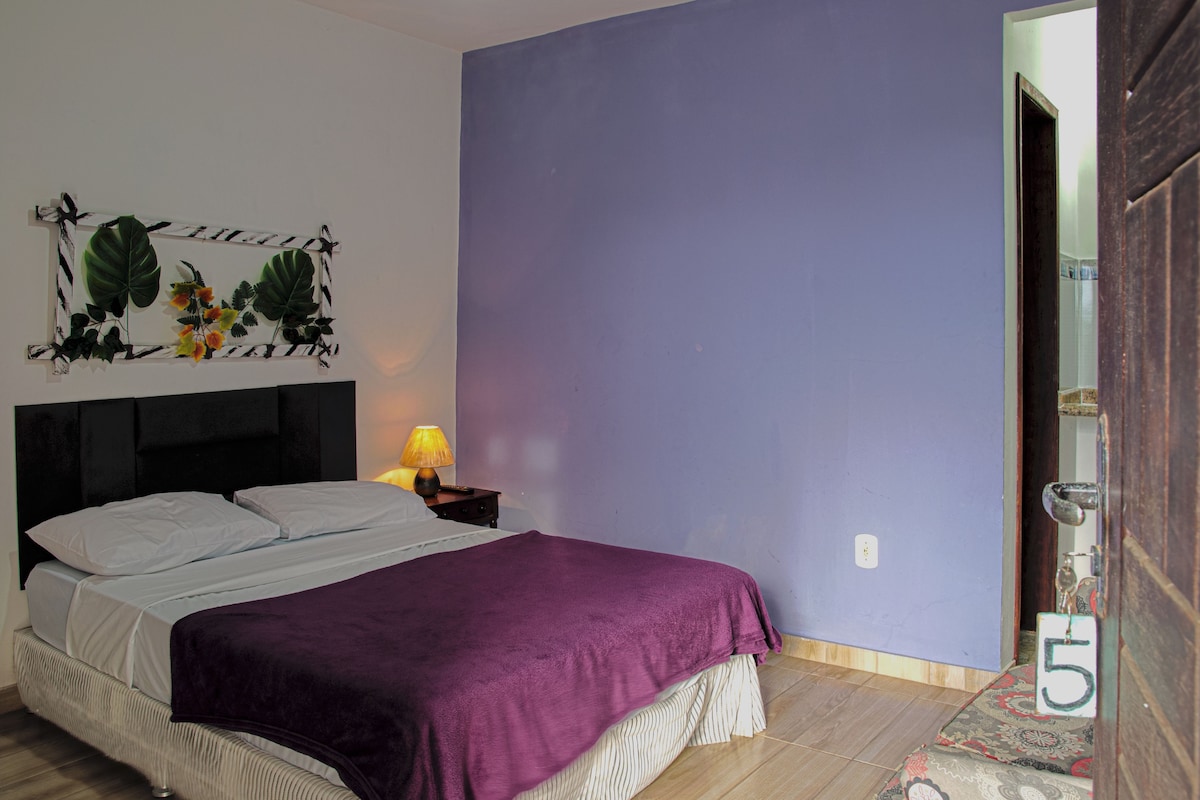 A bedroom with a bed, a nightstand, a lamp, and a door with a number.