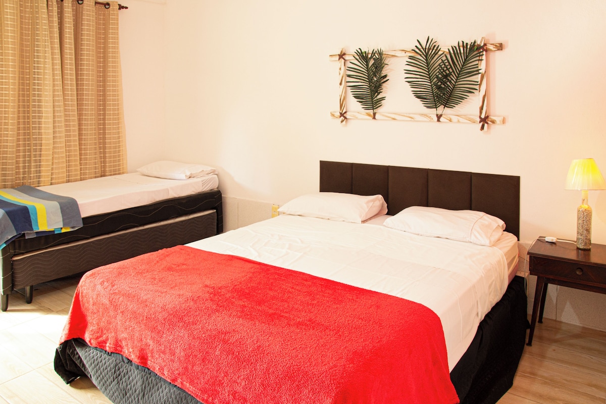 A hotel room with two beds, a red blanket, a nightstand with a lamp, and a wall decoration.