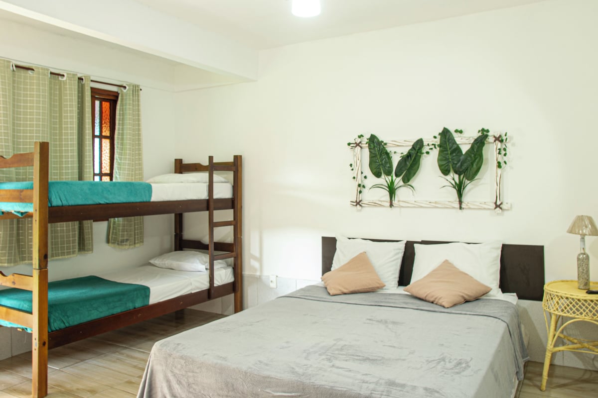 A dormitory room with bunk beds, a single bed, a small table, and a wall-mounted plant decoration.