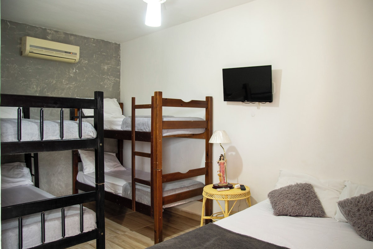 A bunk bed room with a television on the wall, a small table with a lamp, and a bed with pillows.