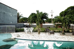 Una piscina con solárium de piedra, rodeada de palmeras y una valla blanca.
