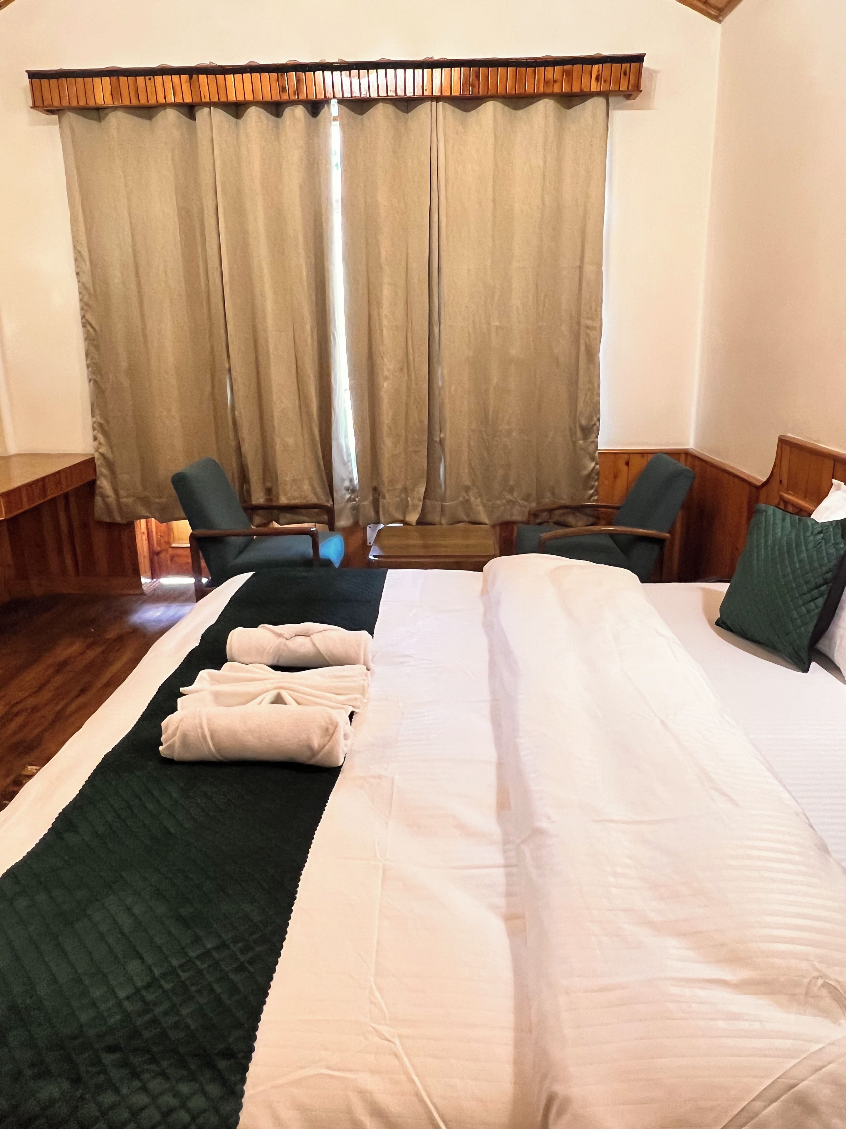 A hotel room with a large bed, two armchairs, a wooden desk, and a window with curtains.