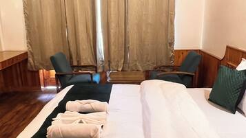 A hotel room with a large bed, two armchairs, a wooden desk, and a window with curtains.