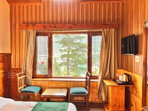 A wooden room with a bed, two chairs, a small table, a TV, and a window with a view of trees.
