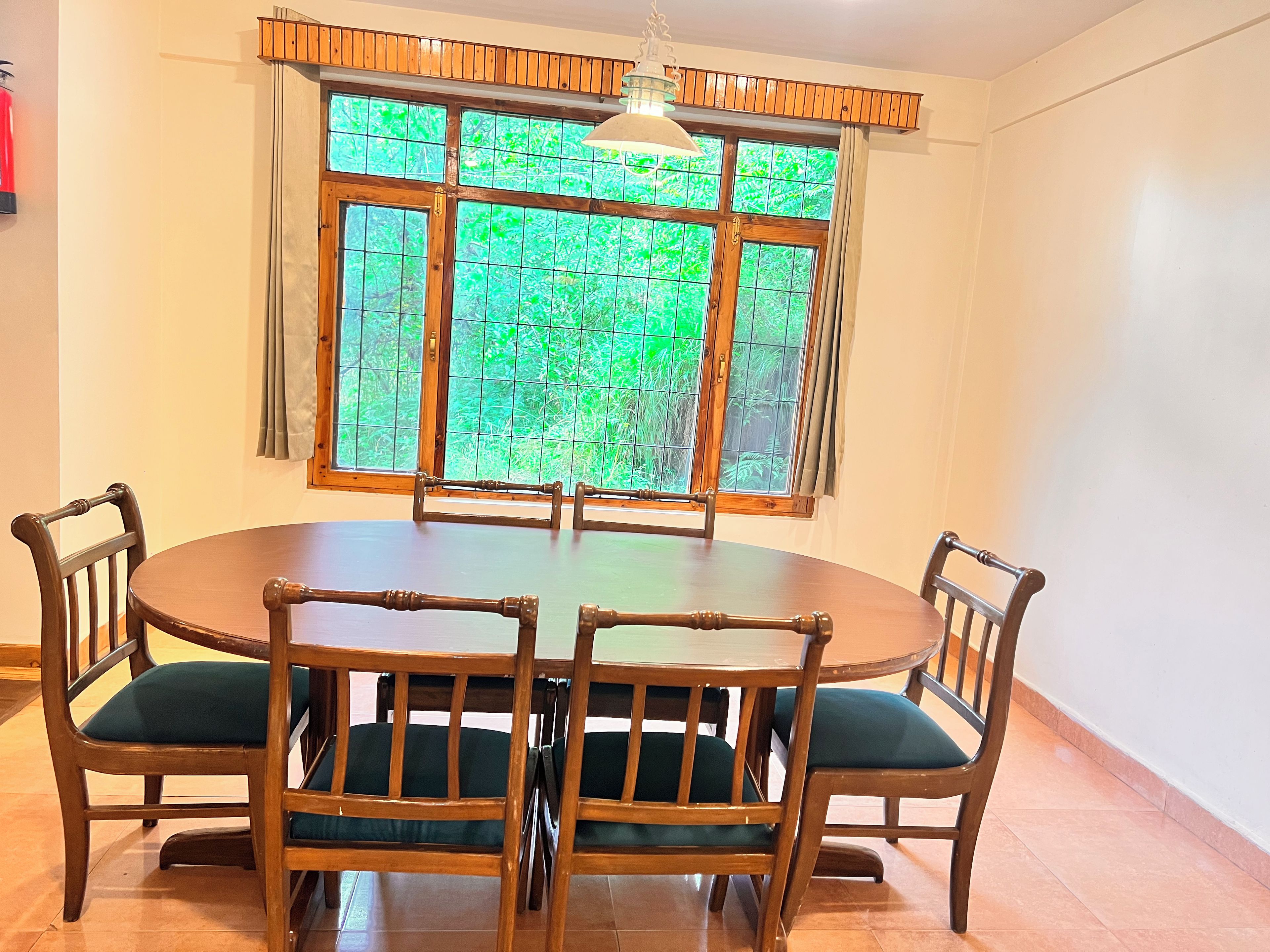 A dining area with a round table and six wooden chairs with green cushions.