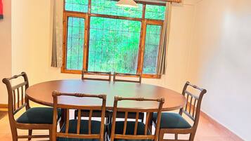 A dining area with a round table and six wooden chairs with green cushions.