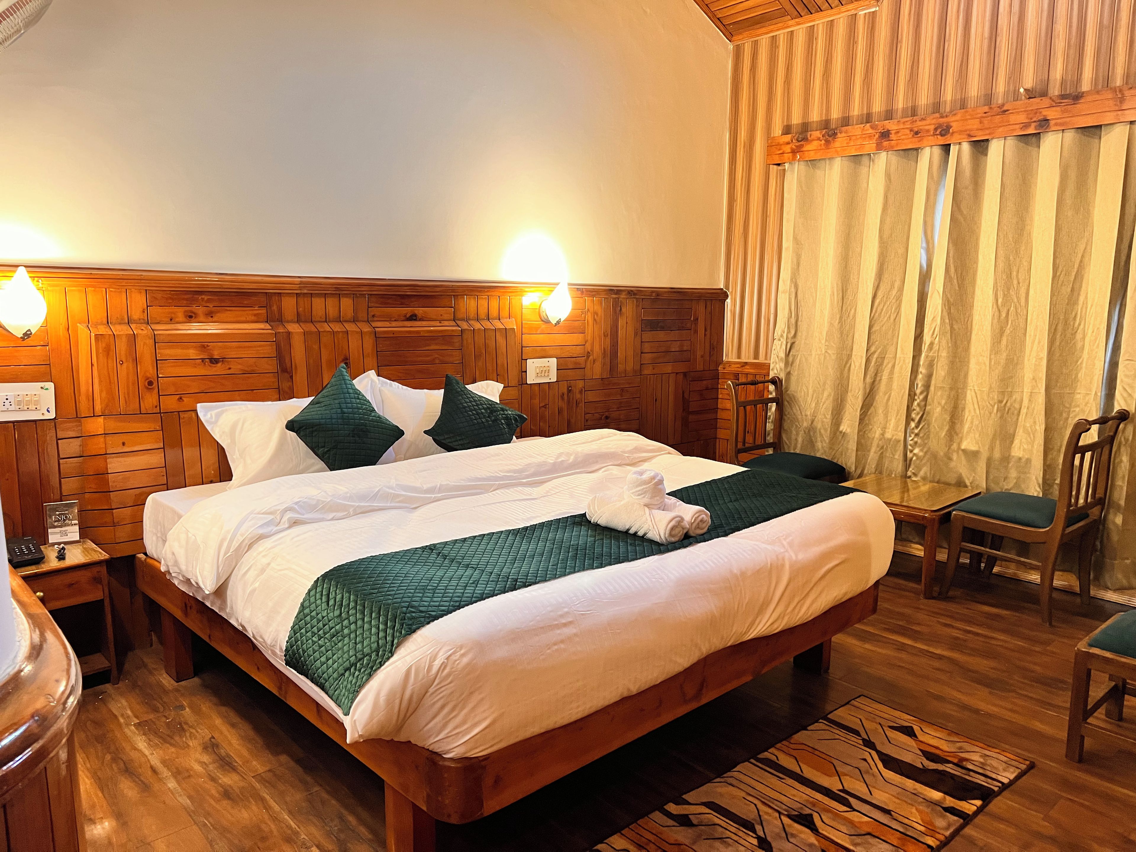 Een kamer met houten lambrisering, een bed, twee bedlampjes, een stoel en een kleine tafel.