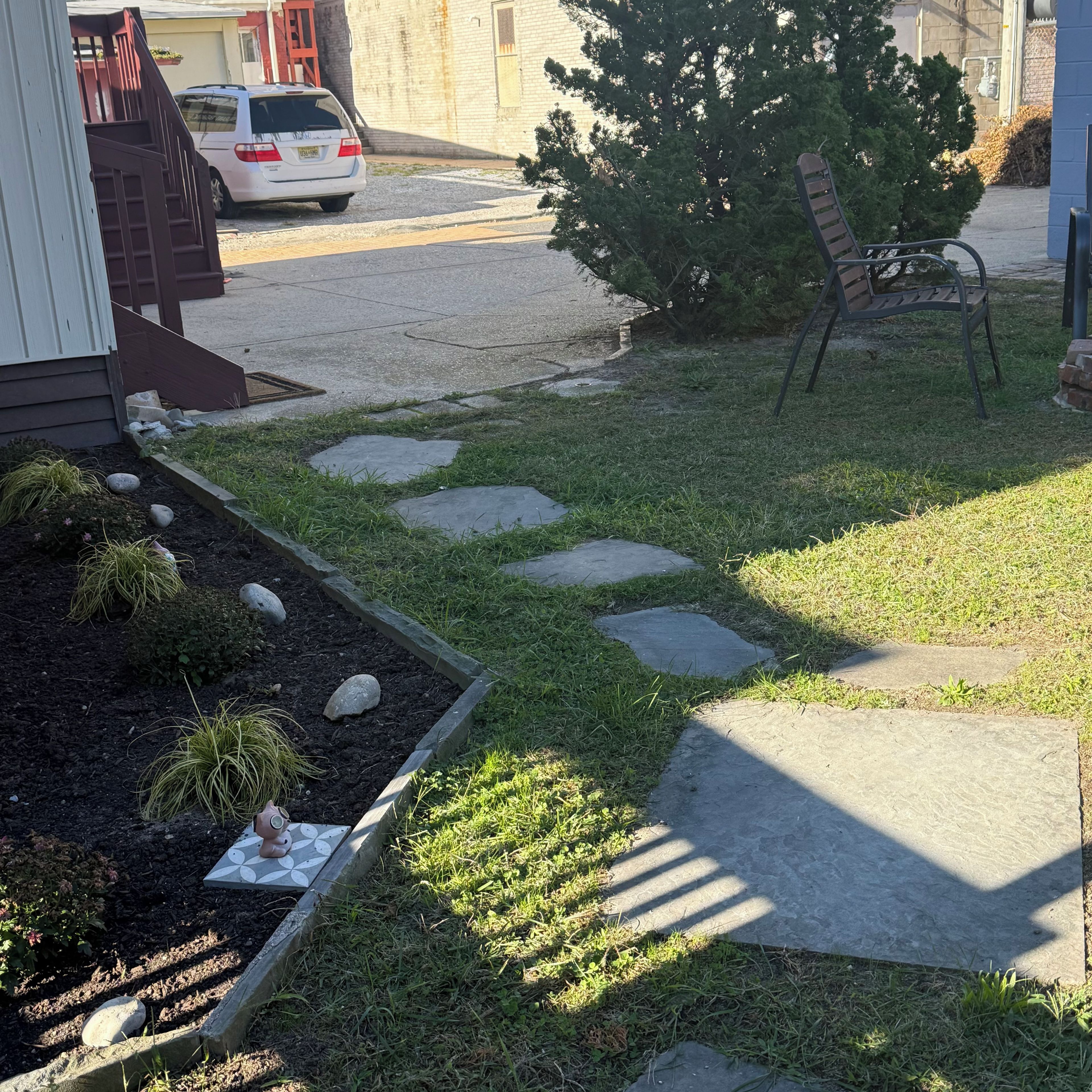 A residential driveway with a stone pathway leading to a house, a parked car, and a small tree.