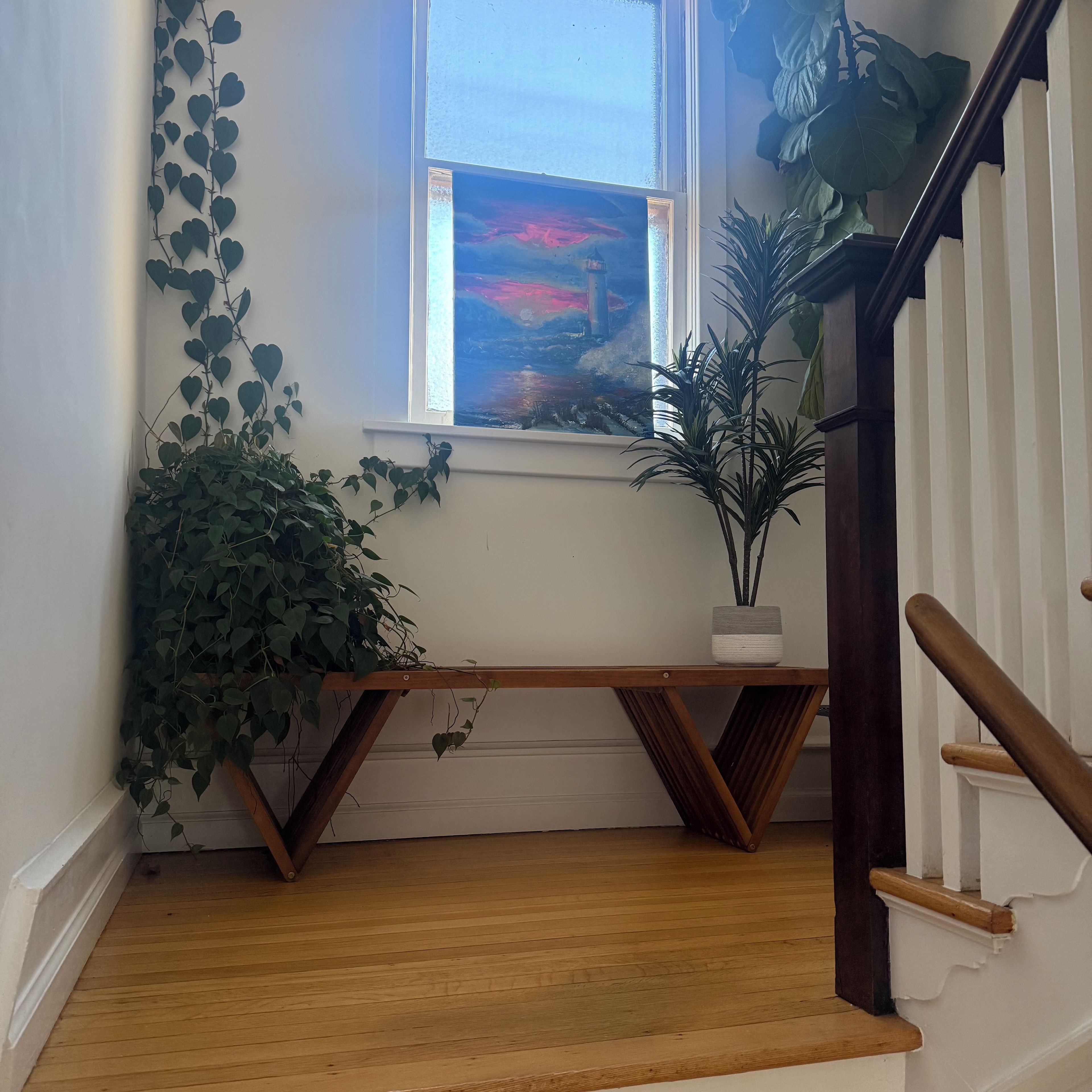 Eine Treppe mit einem hölzernen Geländer, einer weißen Wand und einem Fenster mit einem Gemälde.